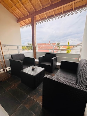 A balcony with wicker furniture, a metal railing, and a view of buildings and a tree.