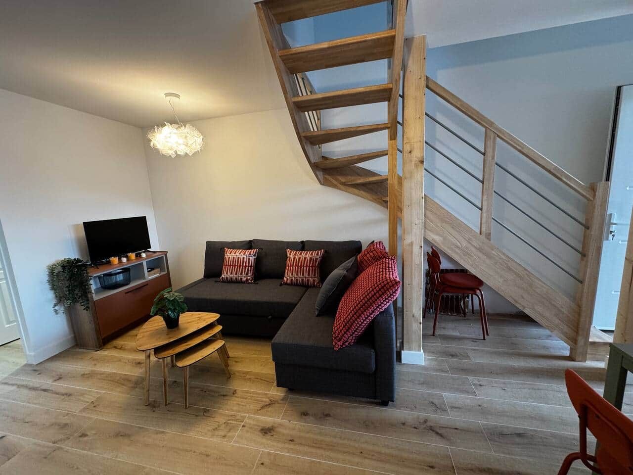 A modern living room with a wooden staircase, a black sofa, a wooden dining table, and a television.