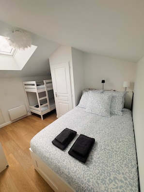 Ein Schlafzimmer mit Etagenbett, einem Bett mit gemusterten Textilien, einem Dachfenster und einer Heizung.