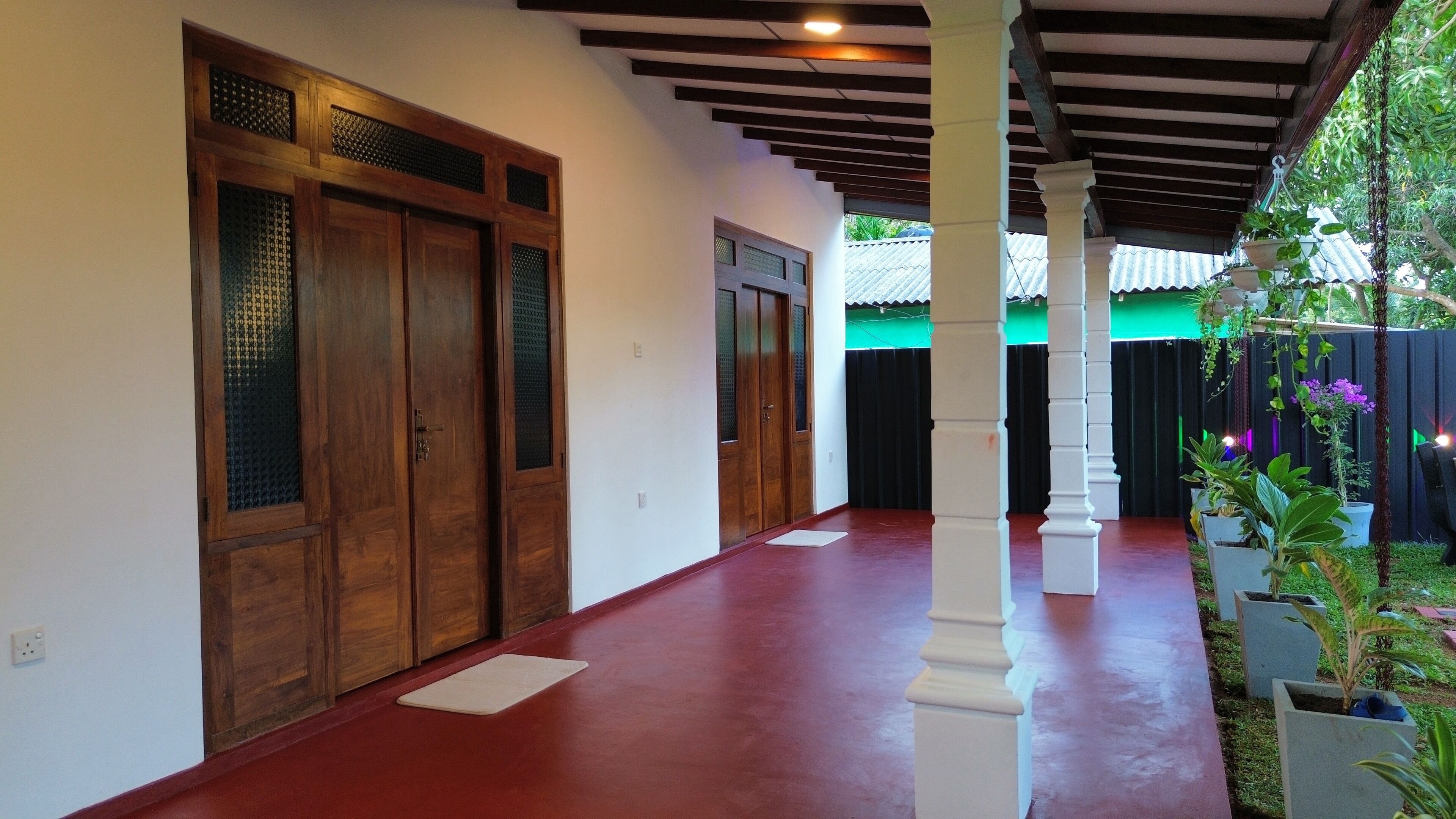 A corridor with wooden doors, white pillars, and potted plants.