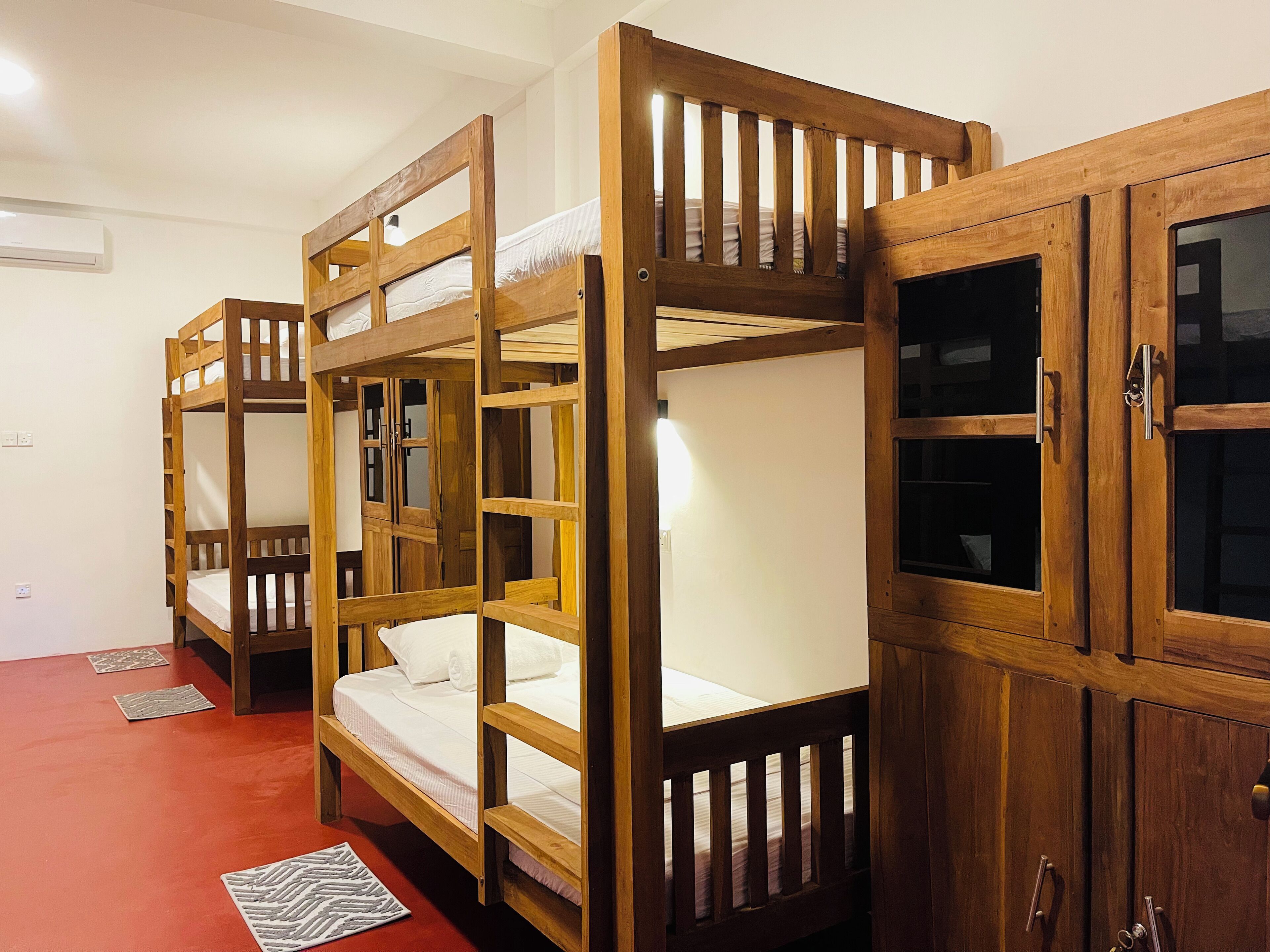 Ein Schlafraum mit Etagenbetten, Holzrahmen, einem roten Boden und einem Schrank mit Glastüren.