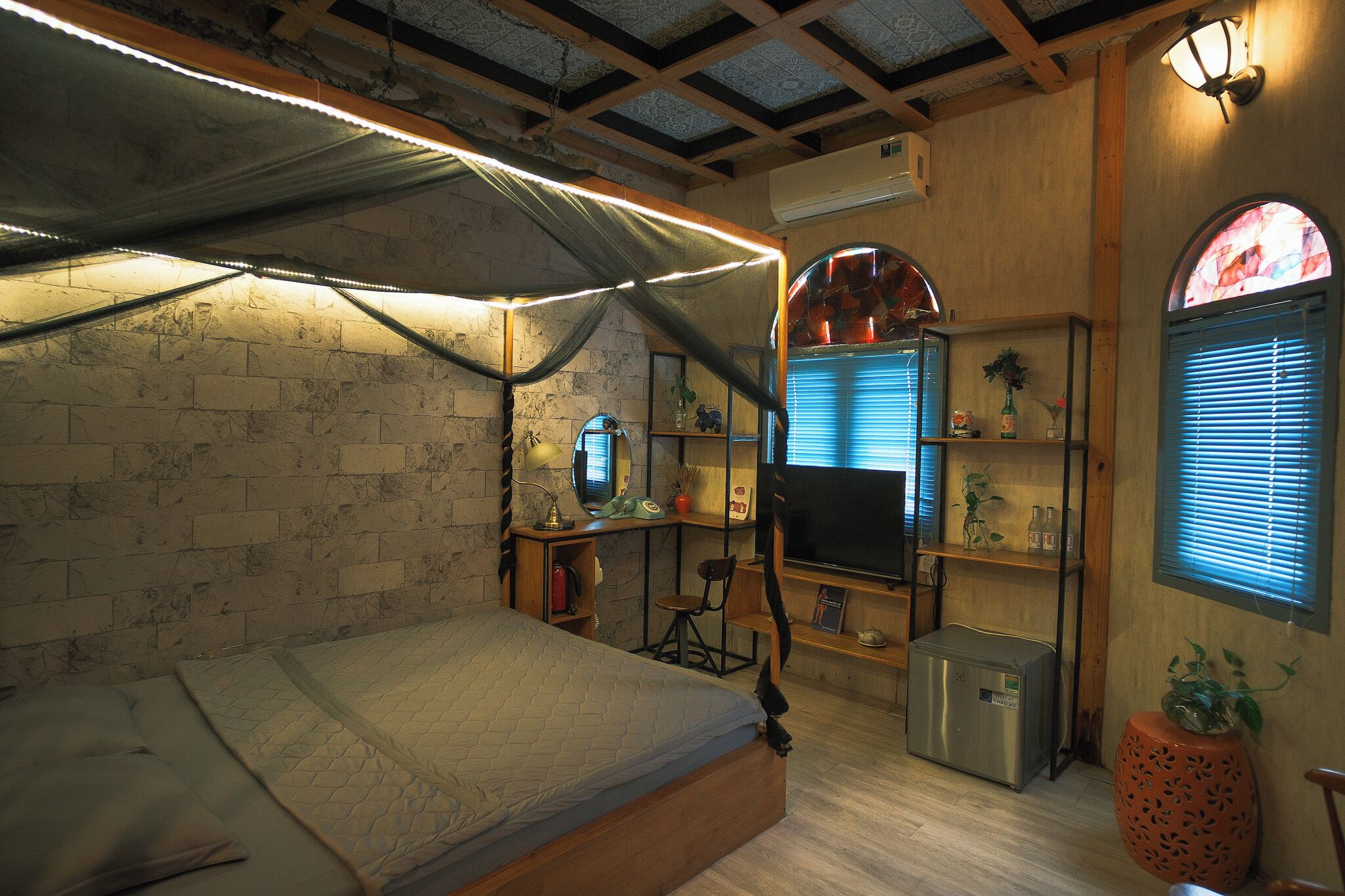 A bedroom with a bed, a desk, a chair, a small refrigerator, and a TV.