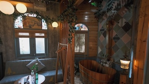 Una habitación acogedora con una bañera de madera, un banco de madera y una mesa con una botella y un control remoto.