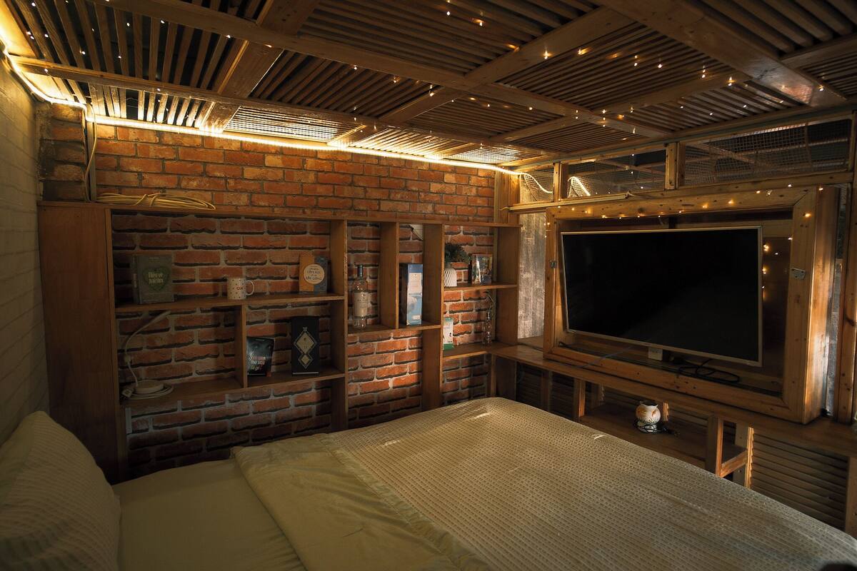 Una habitación con pared de ladrillo, techo de madera y un televisor de pantalla plana grande.