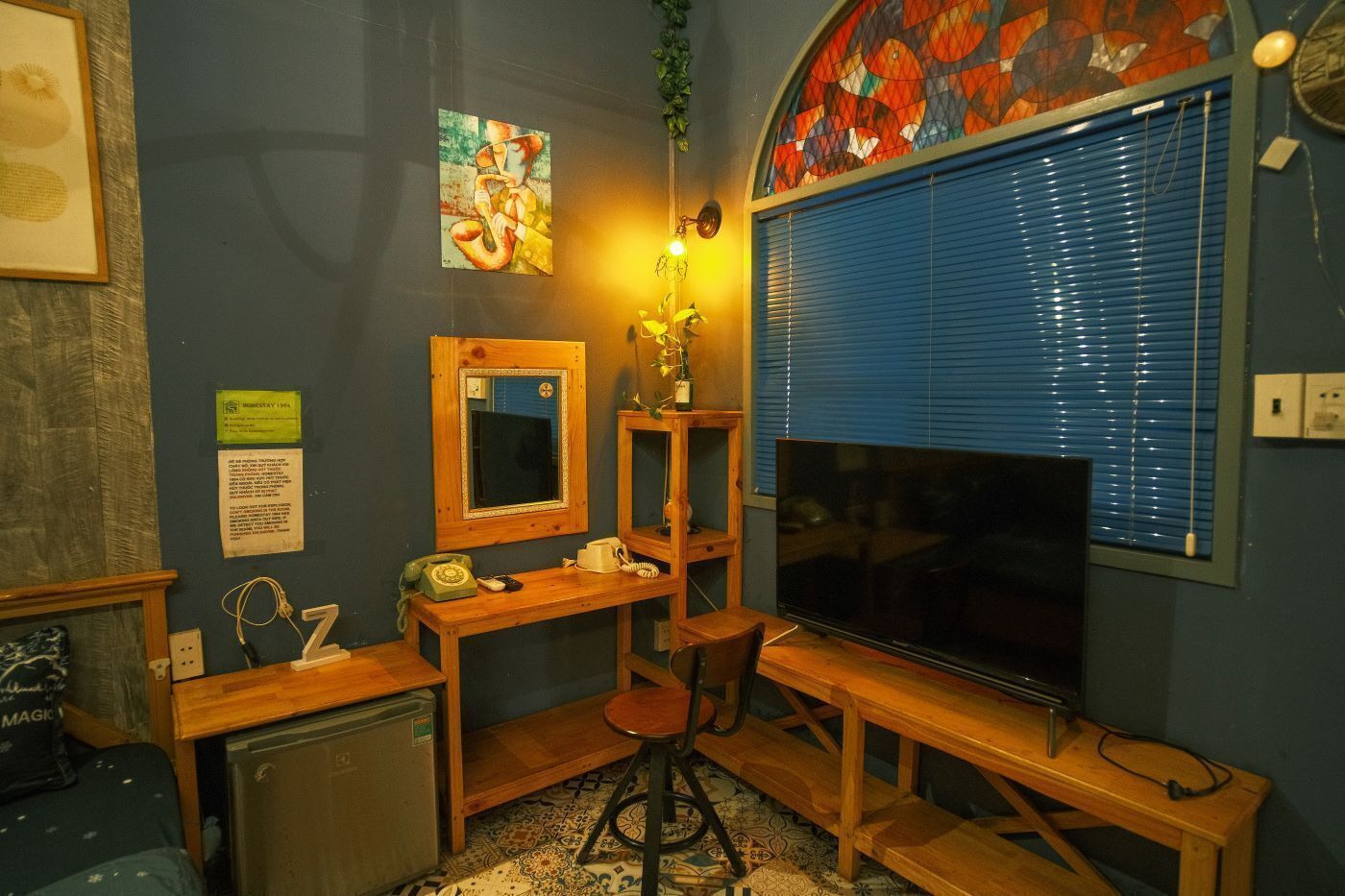 Un espacio de oficina pequeño con escritorio, silla y televisor. Un espejo y un cuadro decoran la pared.