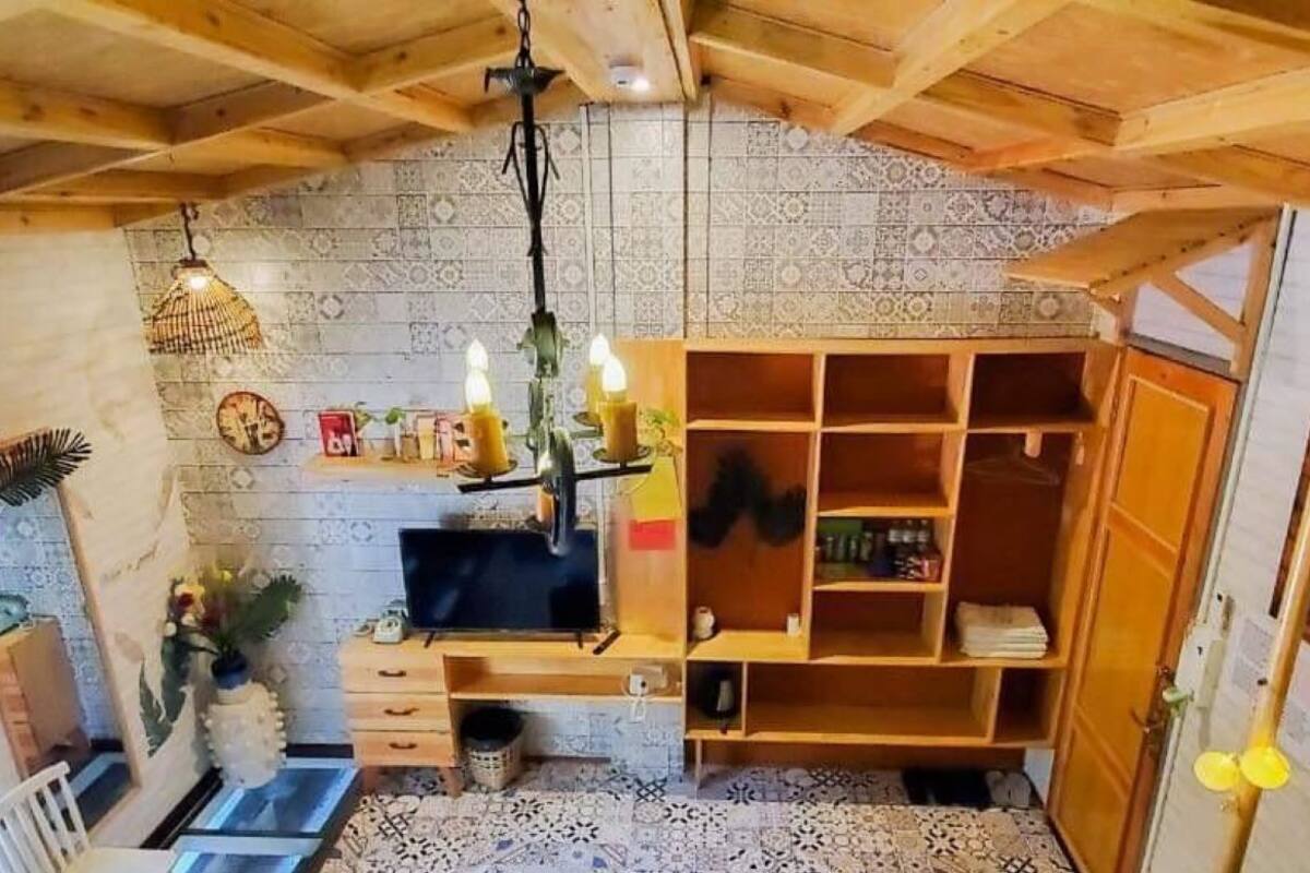 Una habitación acogedora con techo de madera, salpicadero de azulejos, un mueble de madera y un pequeño escritorio con una computadora.