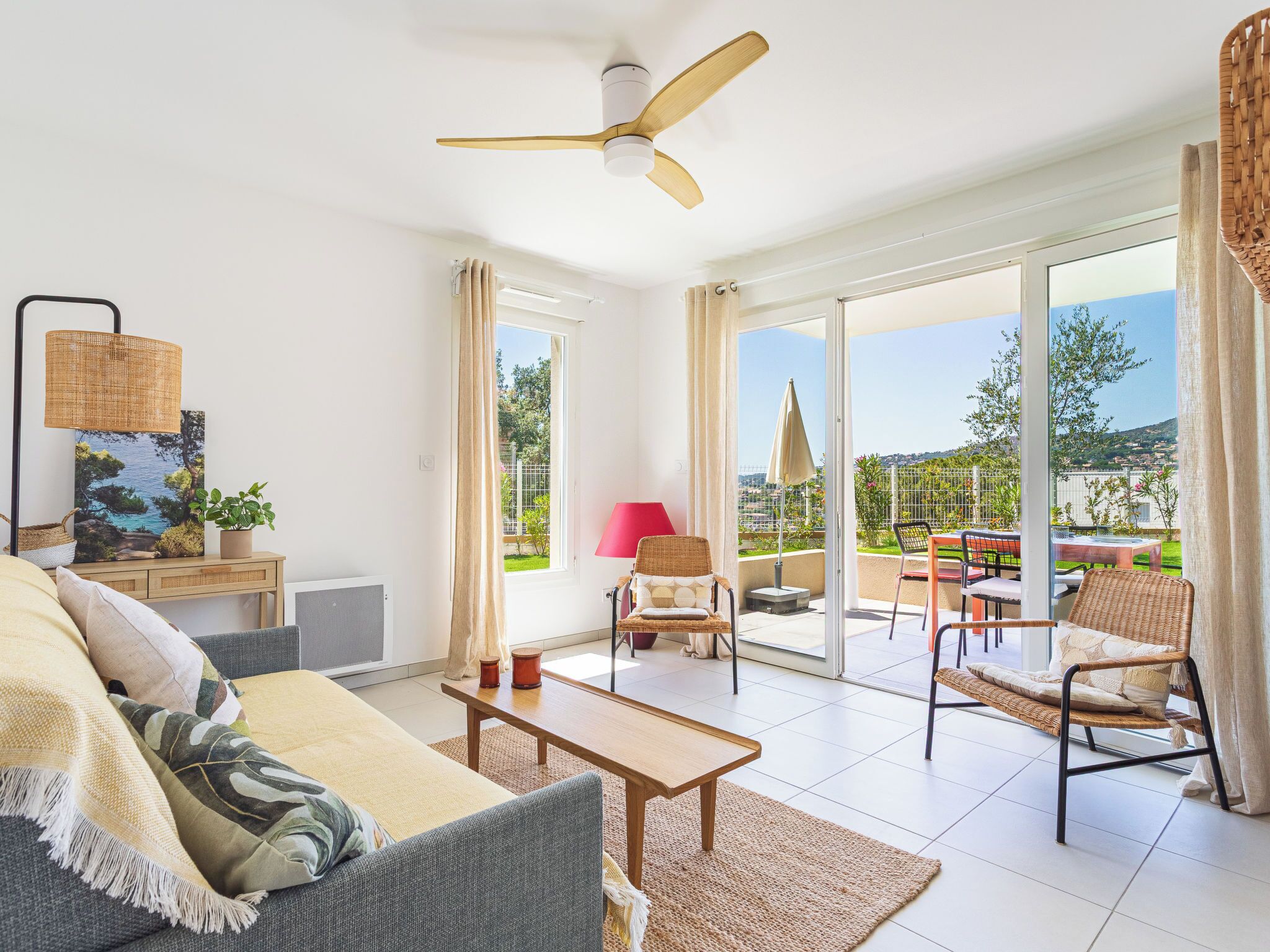 A living room with a sofa, coffee table, and chairs, a ceiling fan, and a view of the outdoors through large sliding doors.