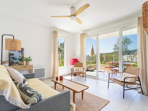 A living room with a sofa, coffee table, and chairs, a ceiling fan, and a view of the outdoors through large sliding doors.