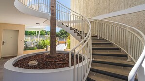 A spiral staircase with a tree in the center, a white railing, and a view of the outdoors.