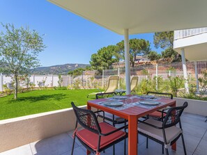 Une terrasse extérieure avec une table dressée pour deux personnes, entourée de chaises, d’une clôture blanche et offrant une vue sur un paysage vallonné.