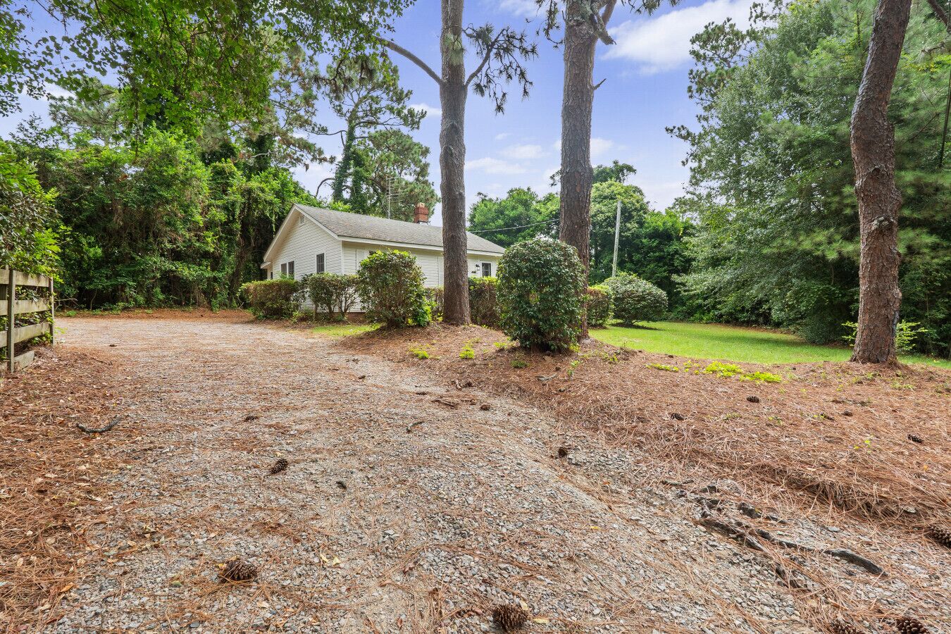 A house with a gravel driveway, surrounded by trees and a grassy yard.