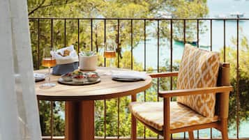 Une table ronde en bois, accompagnée d’une chaise, d’un verre et d’un panier de pain, est placée sur un balcon doté d’une balustrade.