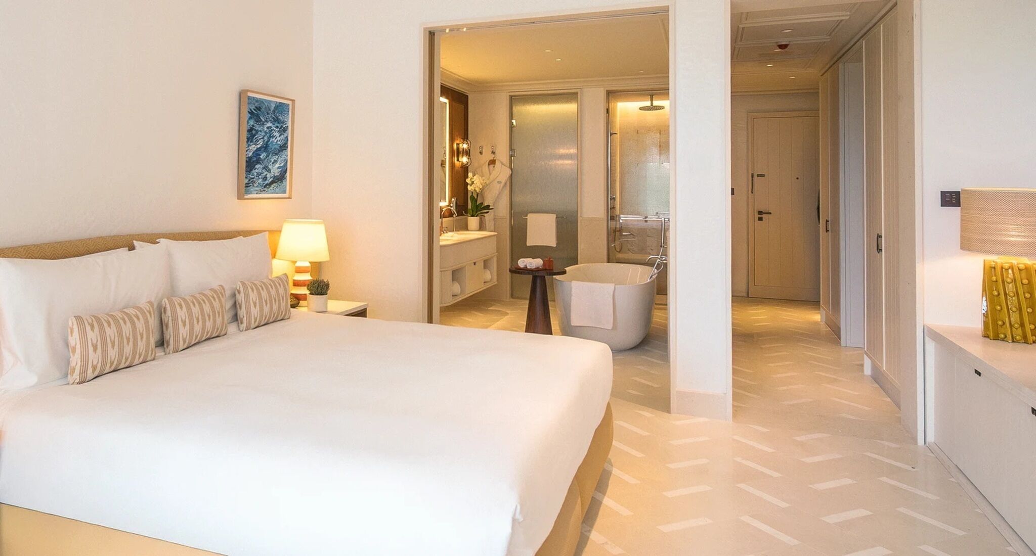 Ett hotellrum med en stor säng, ett badrum med badkar och en hall som leder till andra rum.
