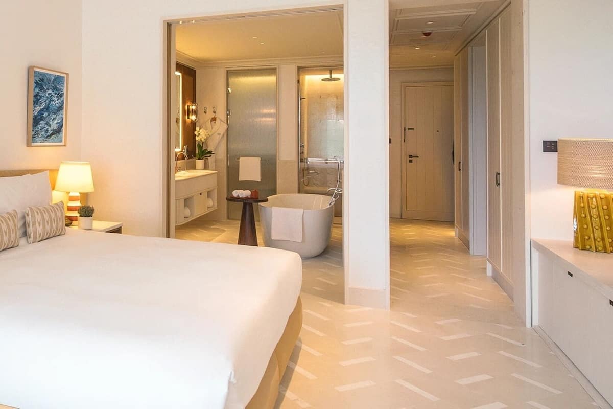Ett hotellrum med en stor säng, ett badrum med badkar och en hall som leder till andra rum.