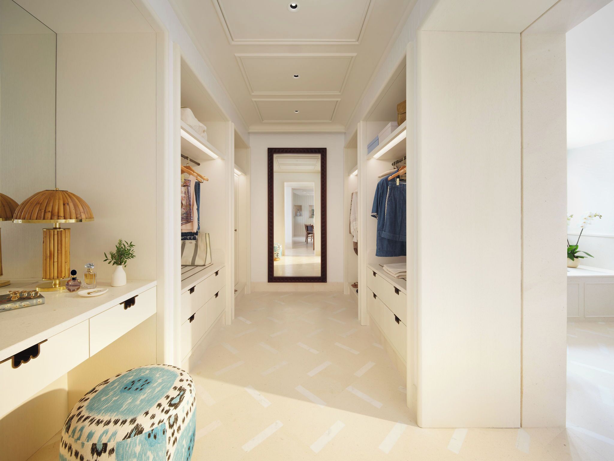 A hallway with a mirrored wardrobe, a vanity with a lamp, and a patterned ottoman.