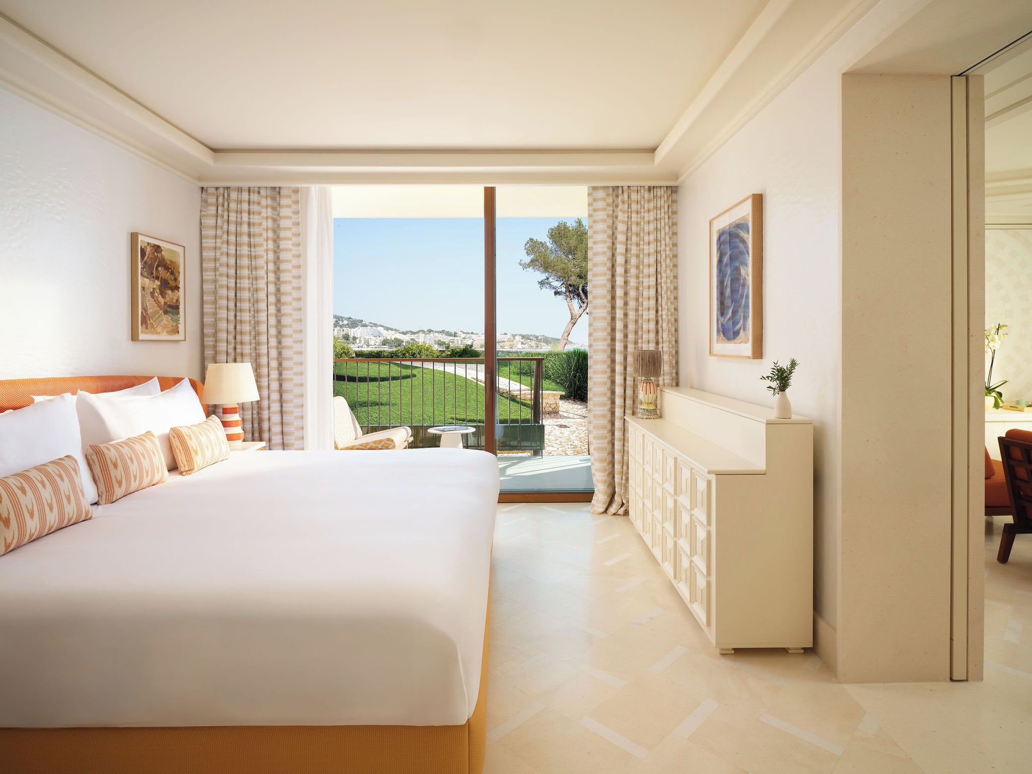 A hotel room with a large bed, a small table, a sofa, a cabinet, and a balcony with a view.