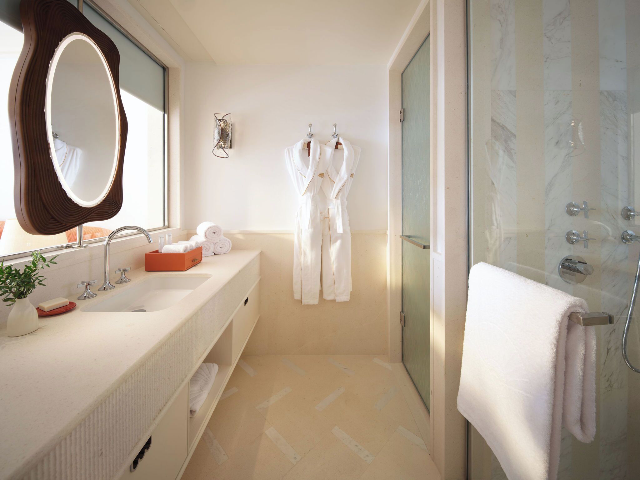 Un baño moderno con un espejo grande, dos lavamanos, cabina de ducha con mampara de cristal y un perchero para toallas.