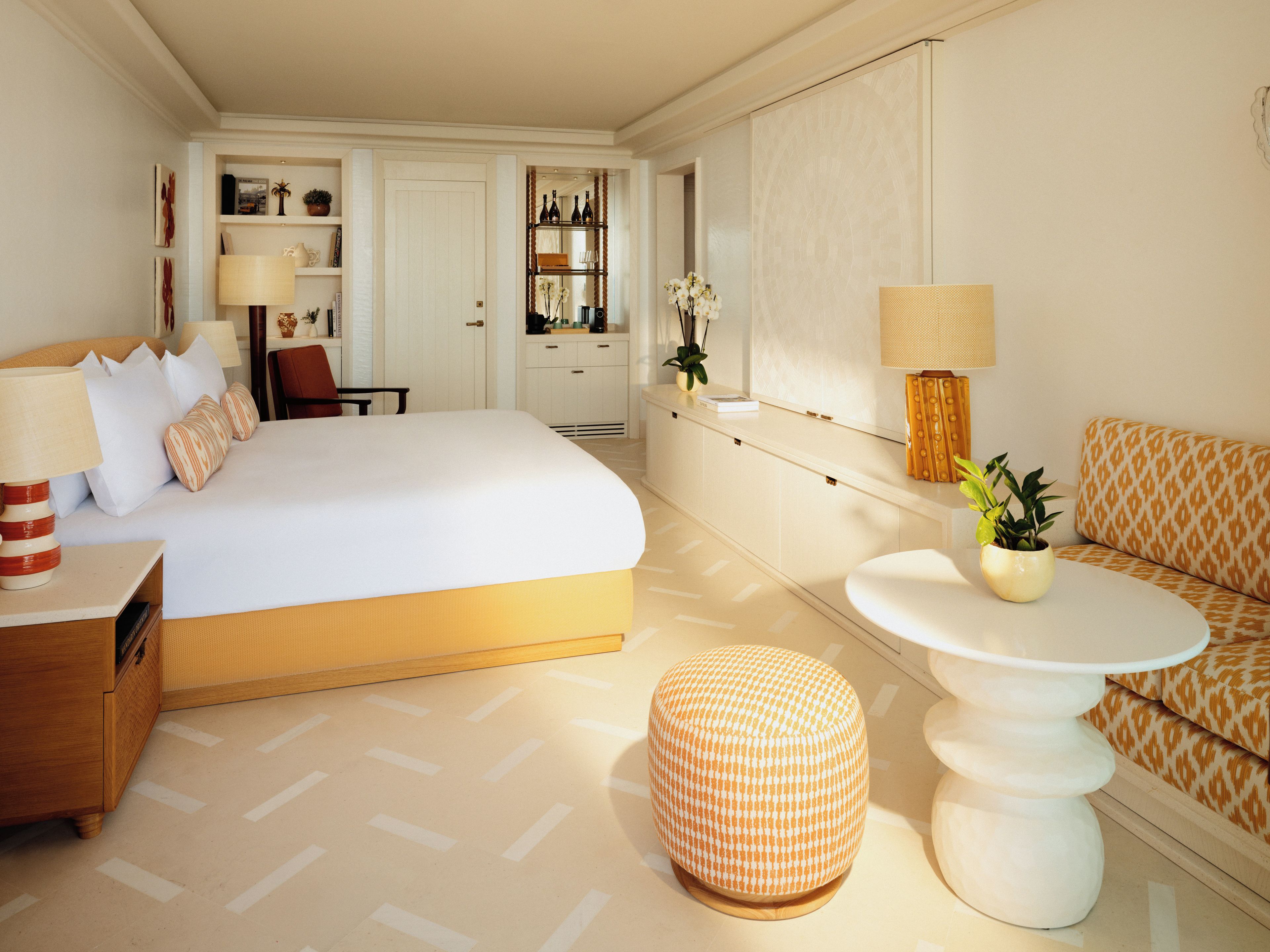 A hotel room with a large bed, a bedside table with a lamp, a sofa, a small round table with a lamp, and a potted plant.