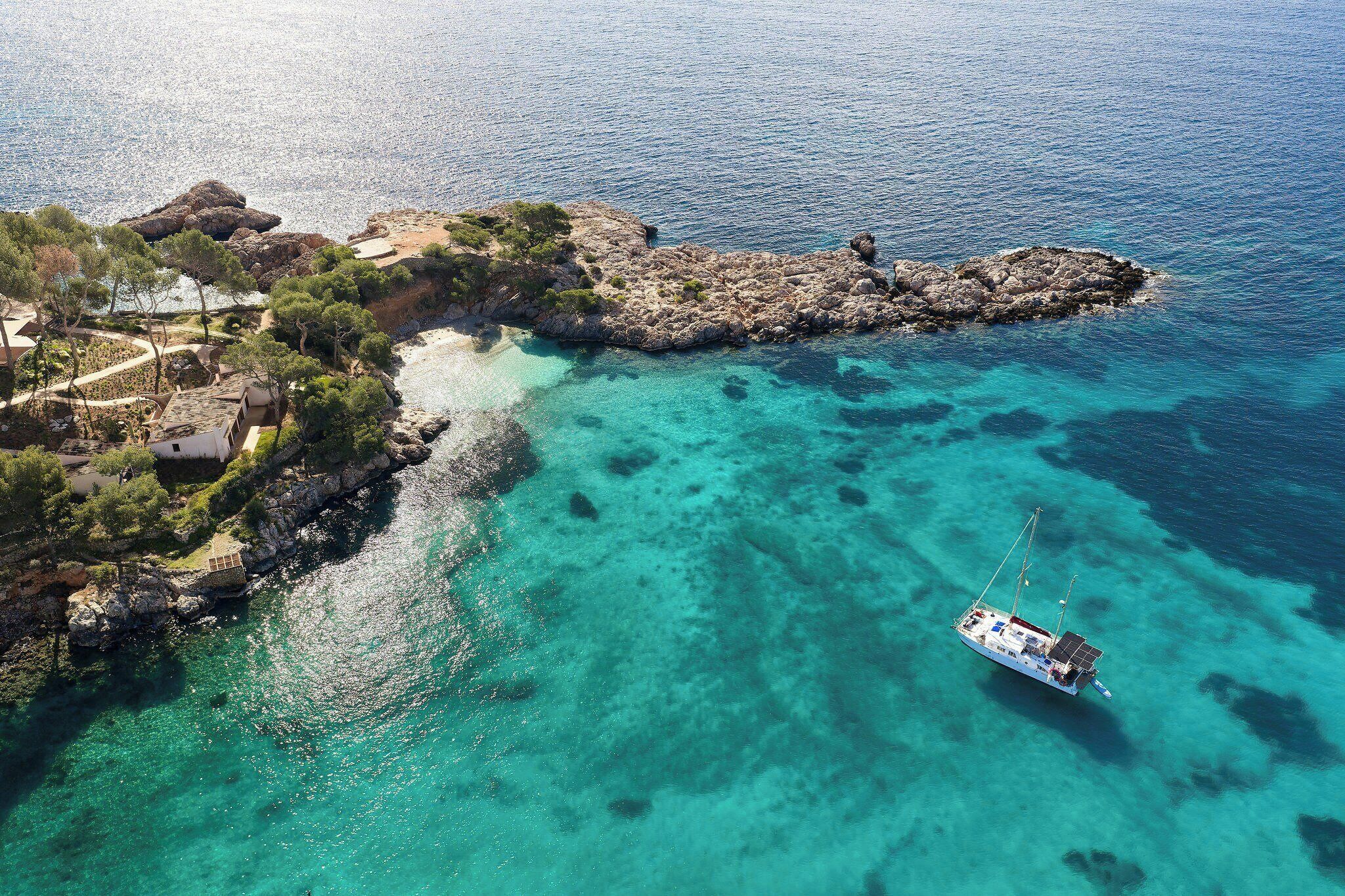 An aerial view of a coastal area with clear turquoise waters, rocky terrain, and a boat anchored near the shore.