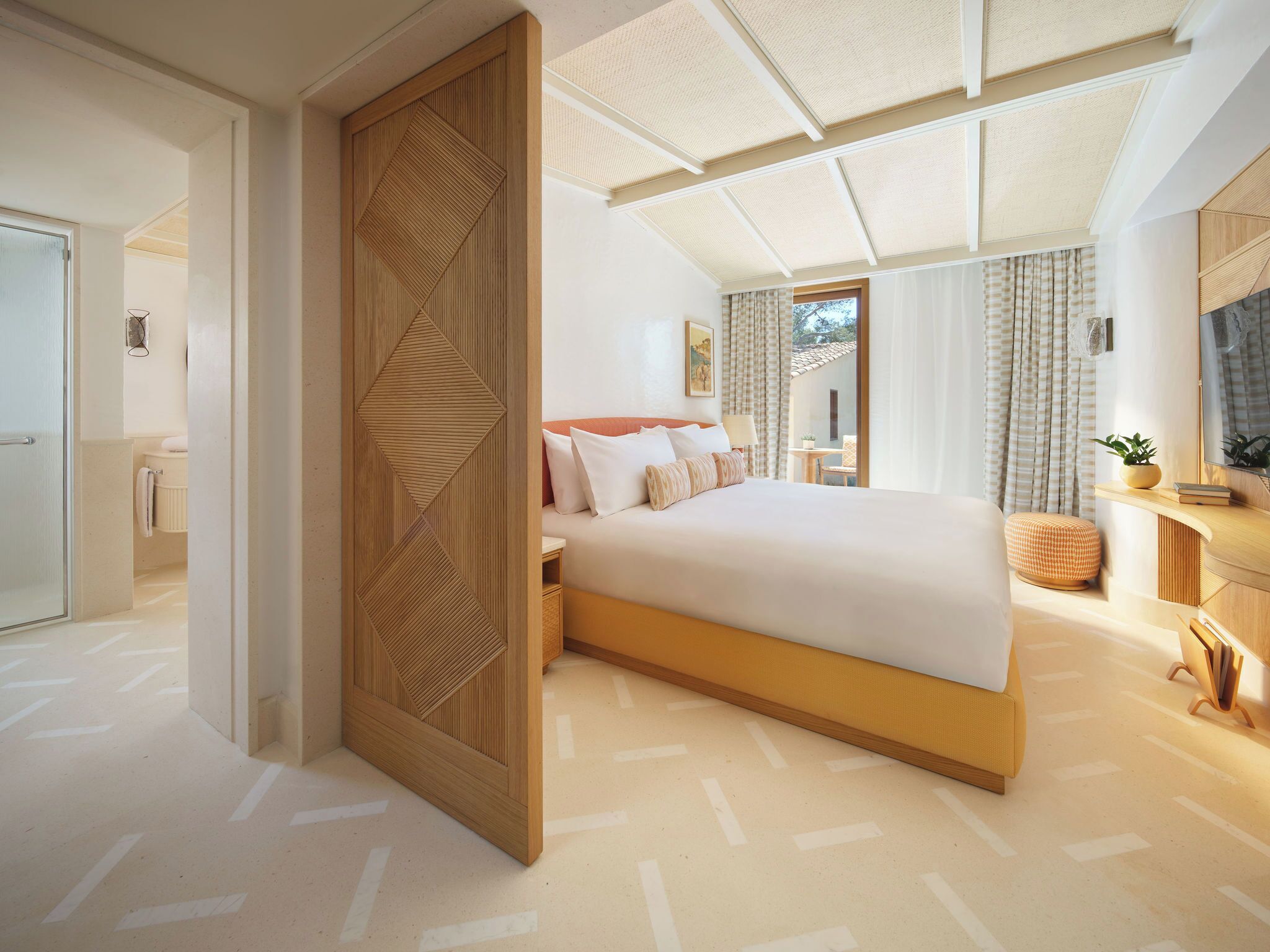Een moderne hotelkamer met een groot bed, een houten scheidingswand, uitzicht op de omgeving en een klein zithoekje.