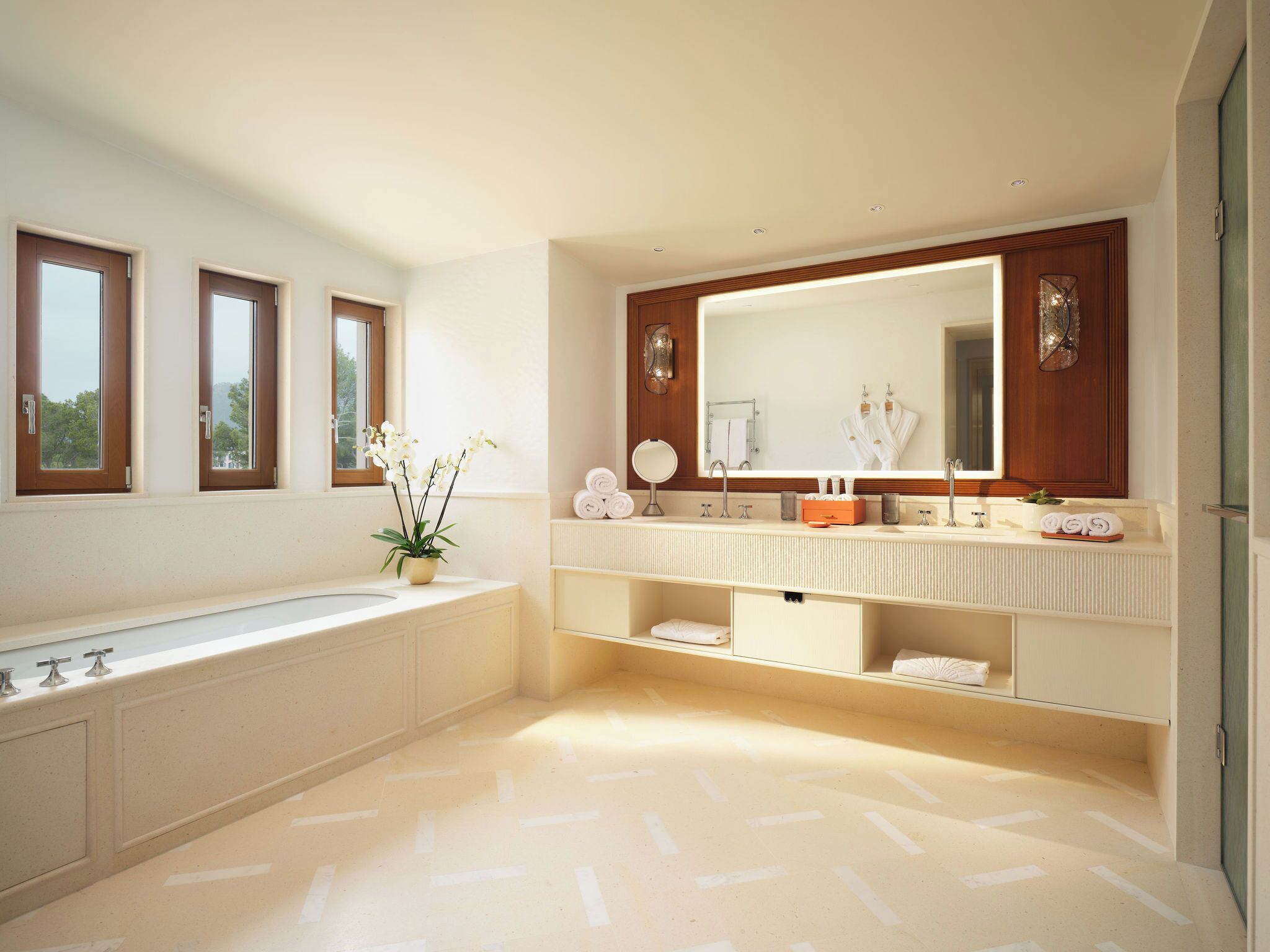 A modern bathroom with a large bathtub, a vanity with a mirror, and a potted orchid.