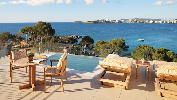Una terraza con piscina, mobiliario exterior y vistas al mar y edificios al fondo.