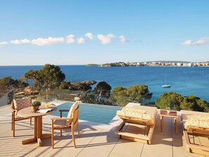 A terrace with a pool, outdoor furniture, and a view of the sea and distant buildings. - Mandarin Oriental Punta Negra, Mallorca (Calvia)