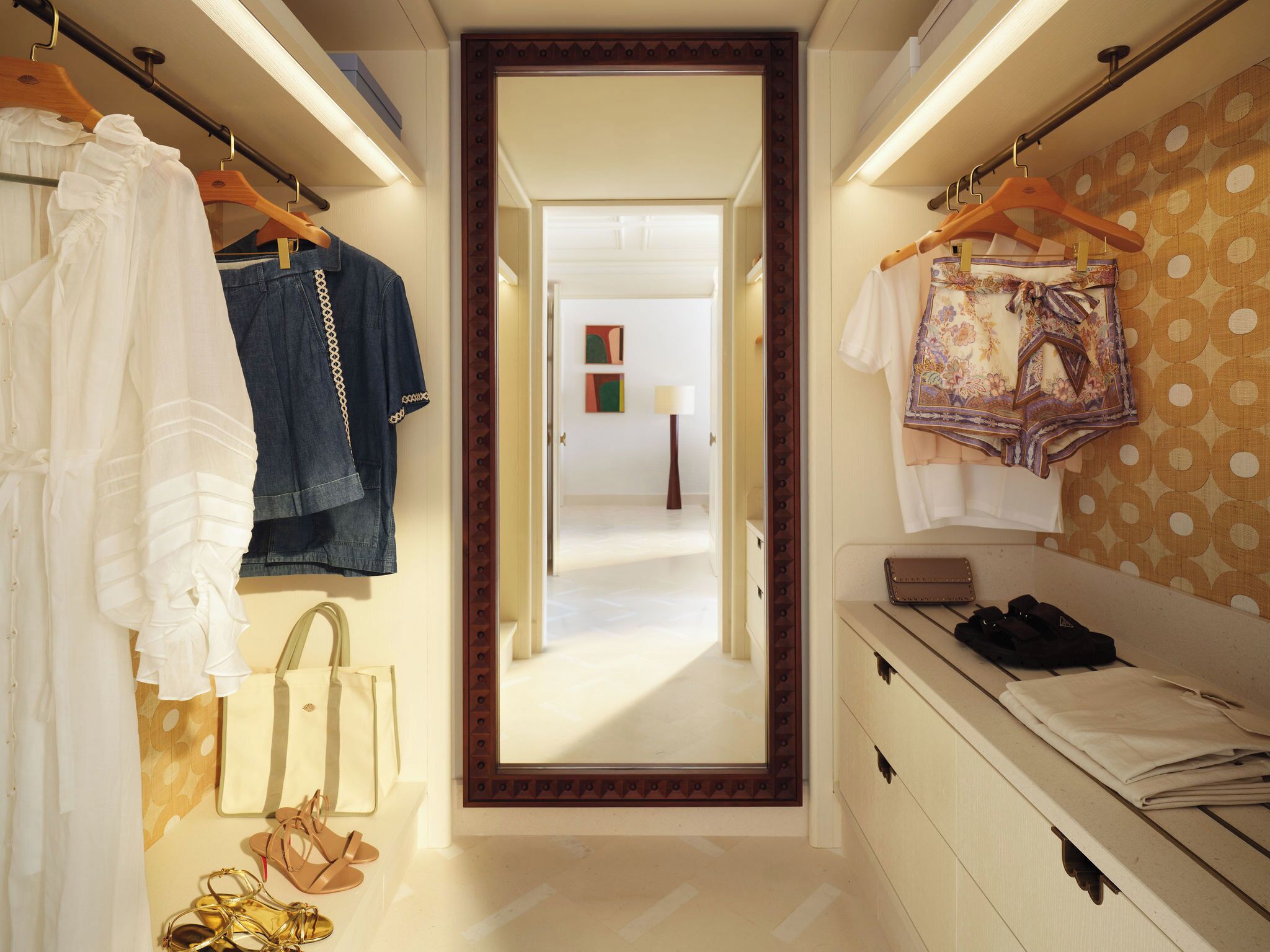 A hallway with clothing racks, a mirror, and a view into another room.