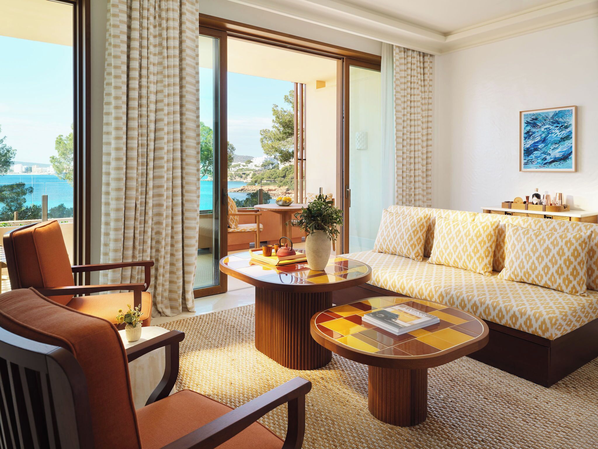 A hotel room with a sofa, armchair, and a table with a vase and magazine.