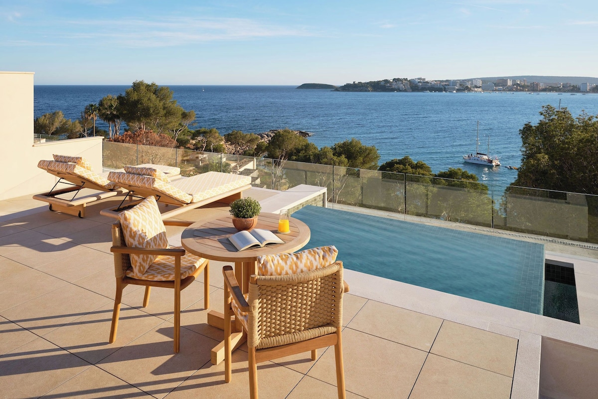 A terrace with lounge chairs, a table, and a pool overlooking the sea.