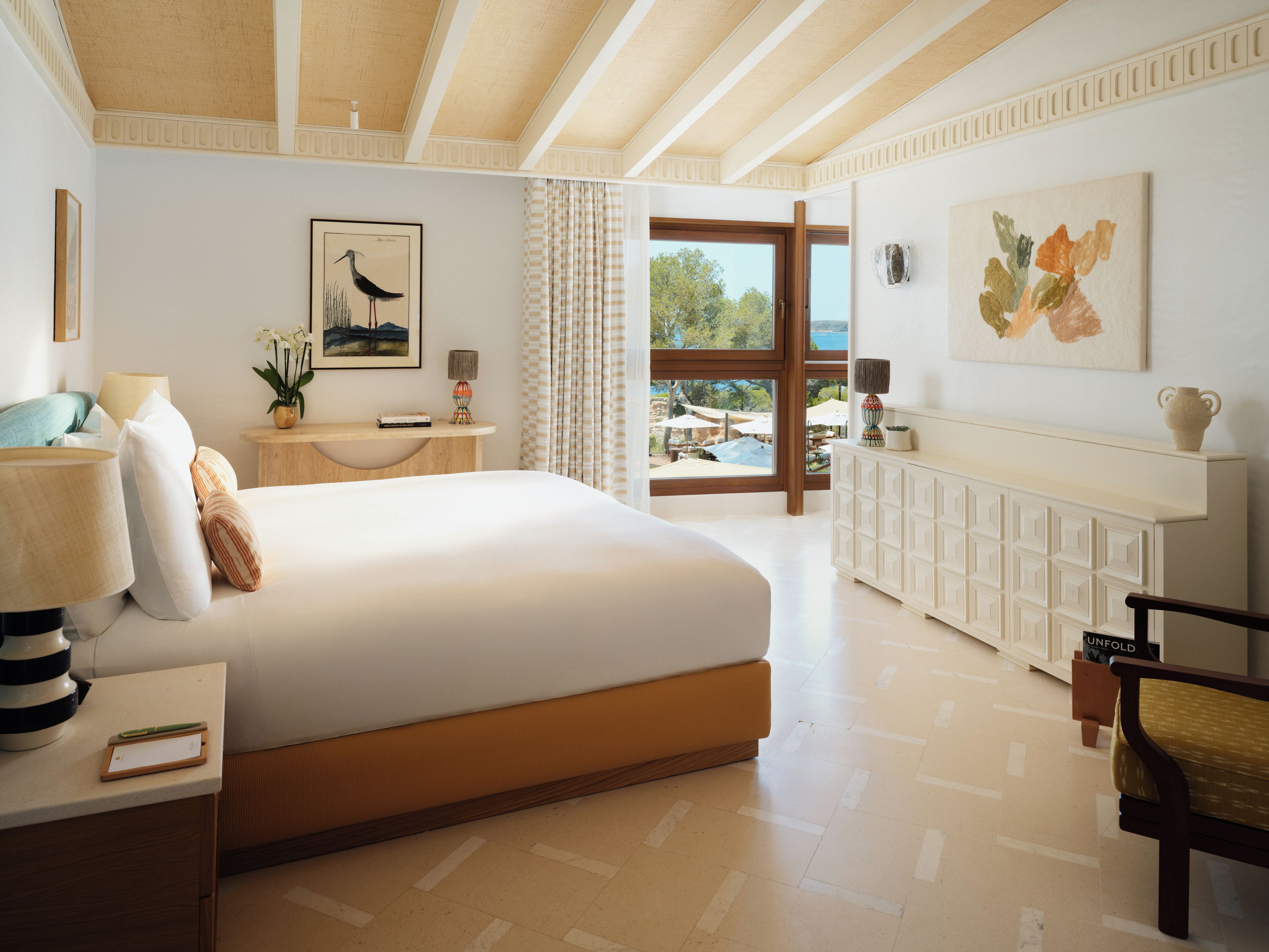Una habitación de hotel con una cama grande, una mesita de noche, un escritorio, una silla, una ventana con cortinas y vistas al exterior.