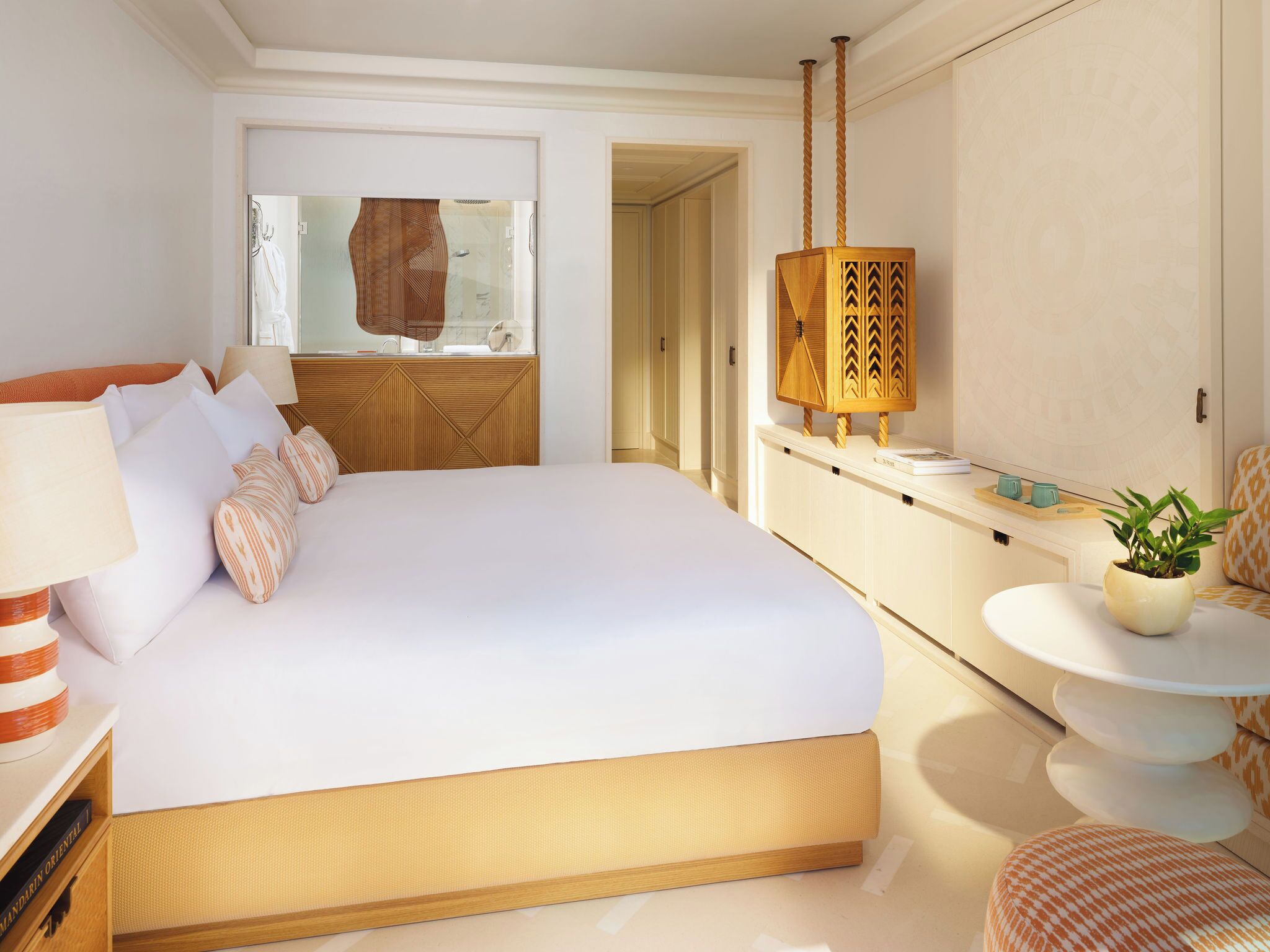 A bedroom with a large bed, a bedside table with a lamp, a small round table with a plant, and a mirror above the bed.