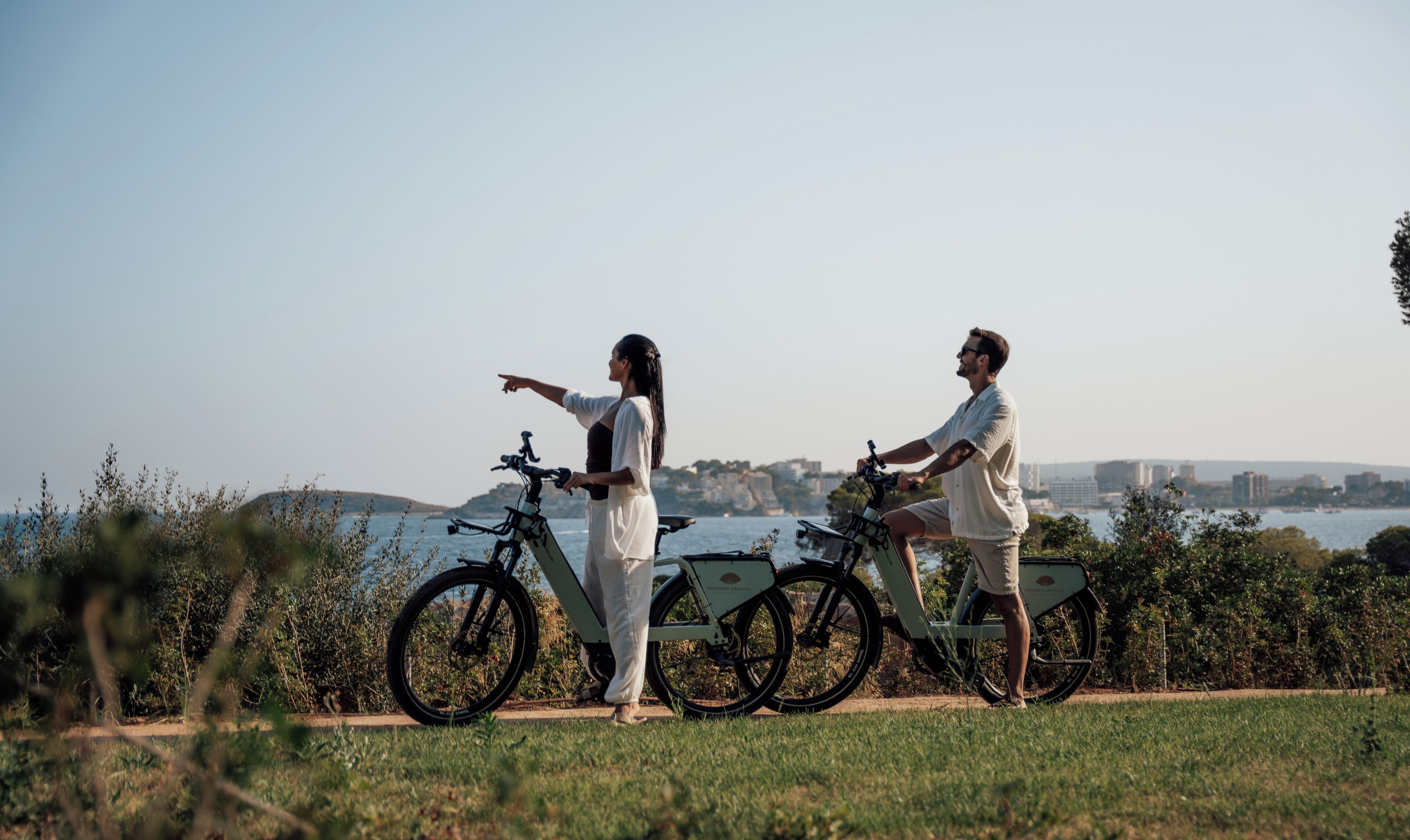 Deux personnes à vélo, avec une vue sur le paysage urbain côtier en arrière-plan.