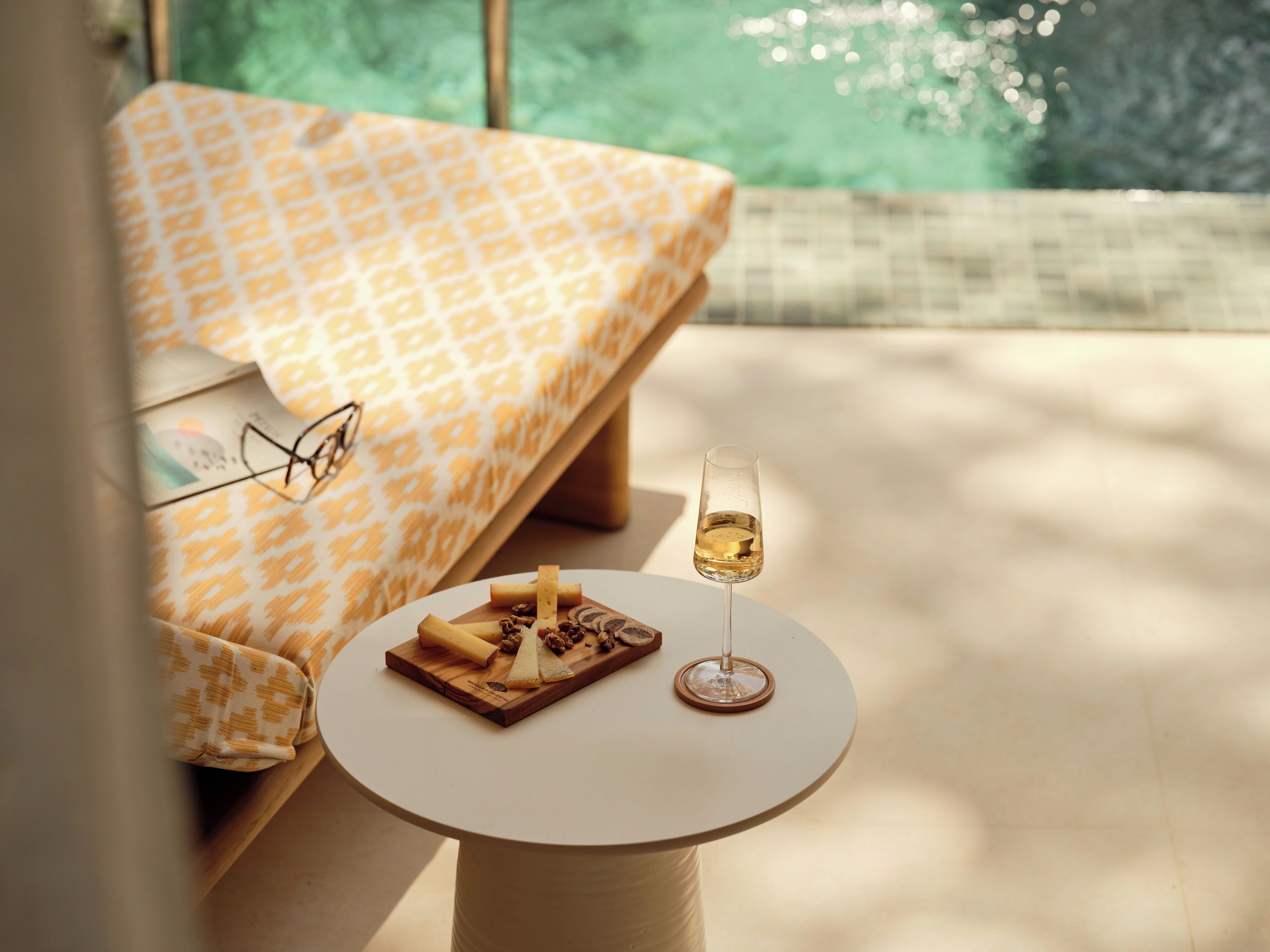 A cozy room with a bed, a small table with a glass of wine, and a wooden board with cheese and crackers.