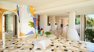 Un vestíbulo amplio con piso de diseño geométrico, una mesa blanca central con jarrones decorativos y un mural abstracto y colorido en la pared.