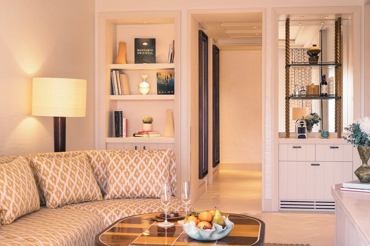 Una sala de estar moderna con un sofá, una mesa de centro con fruta, una lámpara y una estantería con libros y objetos decorativos.