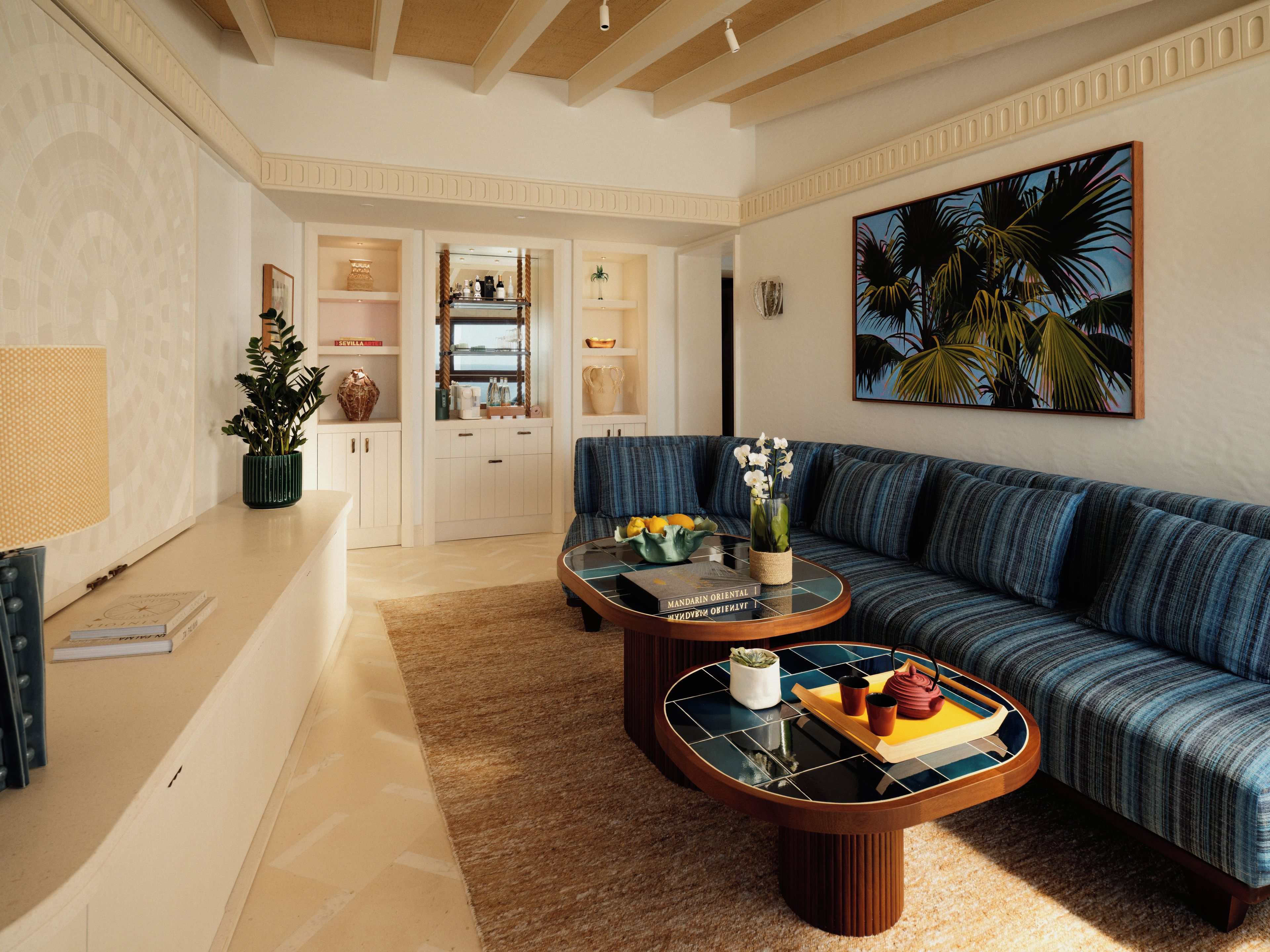 A living room with a blue sofa, a coffee table with a vase and fruit, and a bookshelf with books and decorative items.
