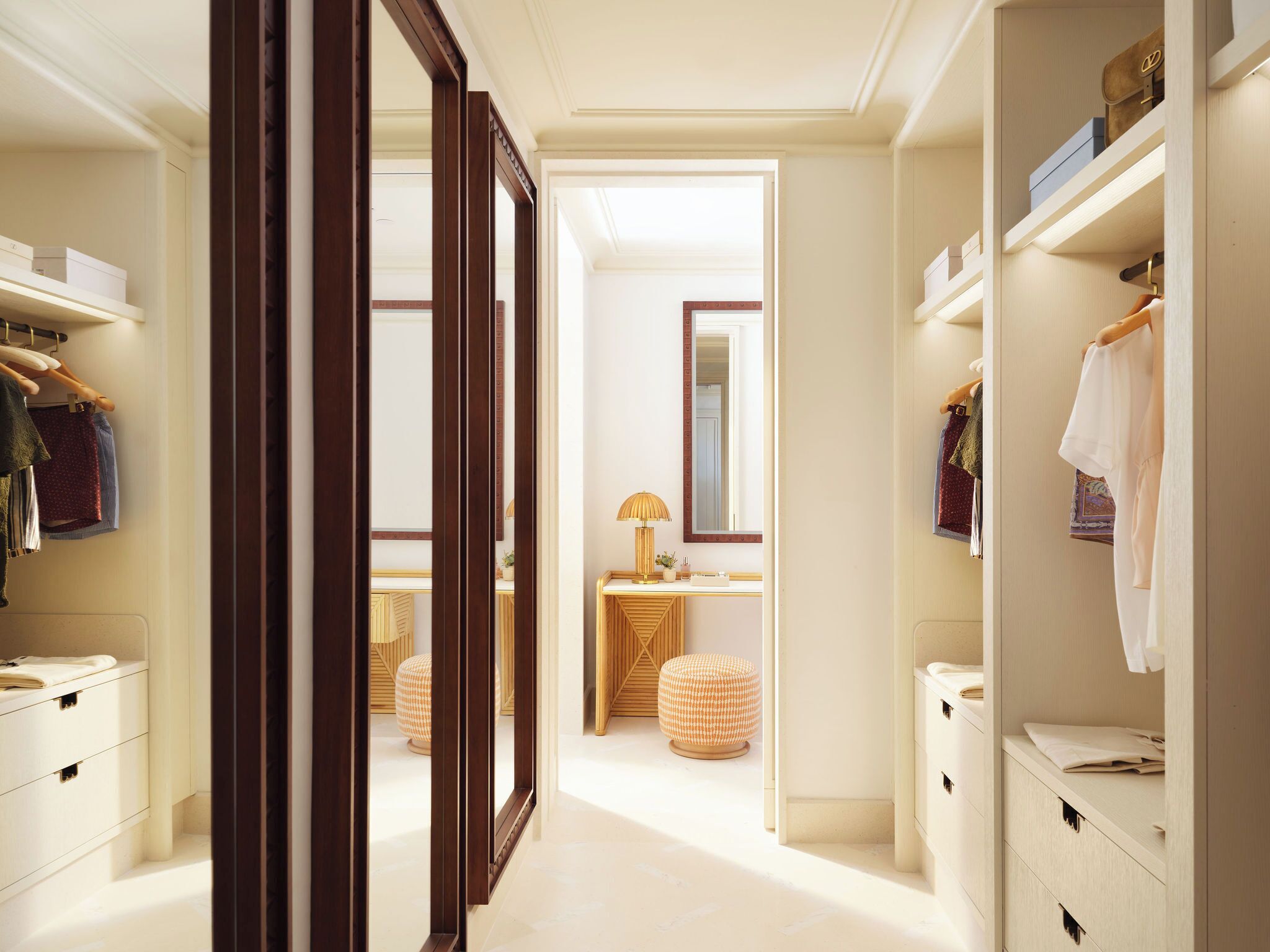 Un couloir avec un cadre de porte en bois, une coiffeuse avec un miroir et un lit à l’arrière-plan.