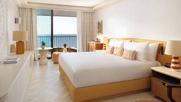 A hotel room with a large bed, a desk, a chair, a small table, and a view of the sea.
