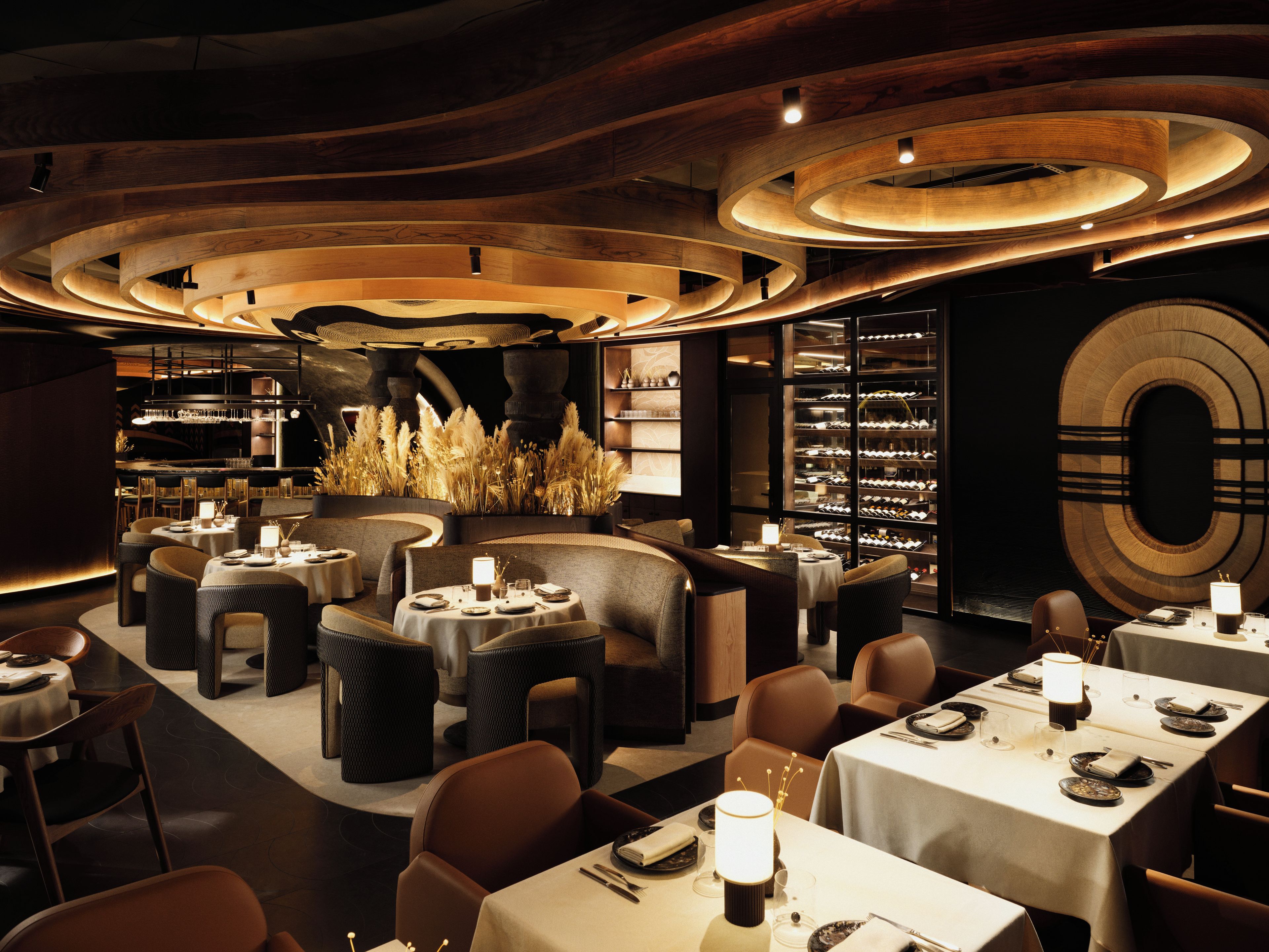 A modern restaurant interior with round tables, leather seating, and a wine cellar.