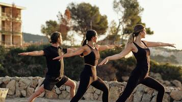 Three people performing a dance on a stone surface outdoors with a building and trees in the background.