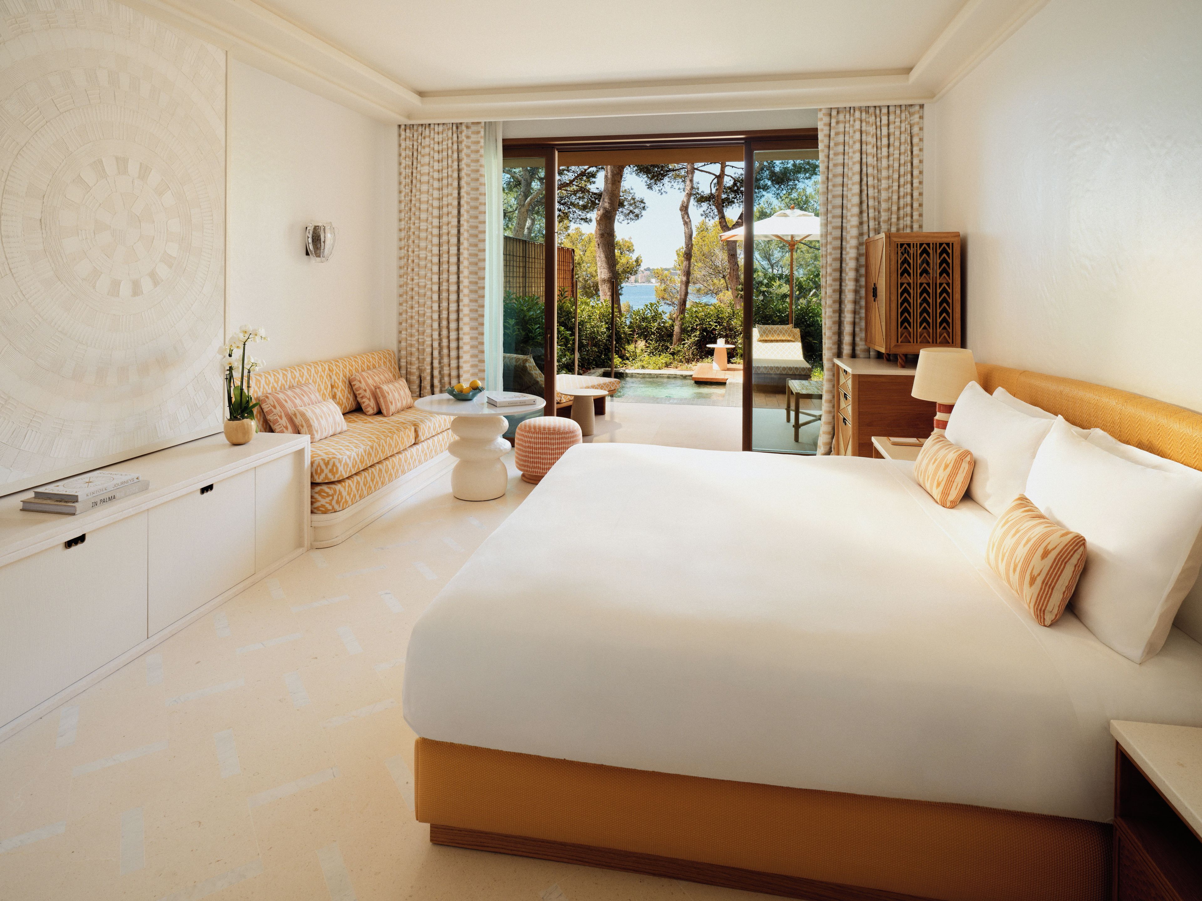 A hotel room with a large bed, a sofa, a dining table, and a view of the outdoors.