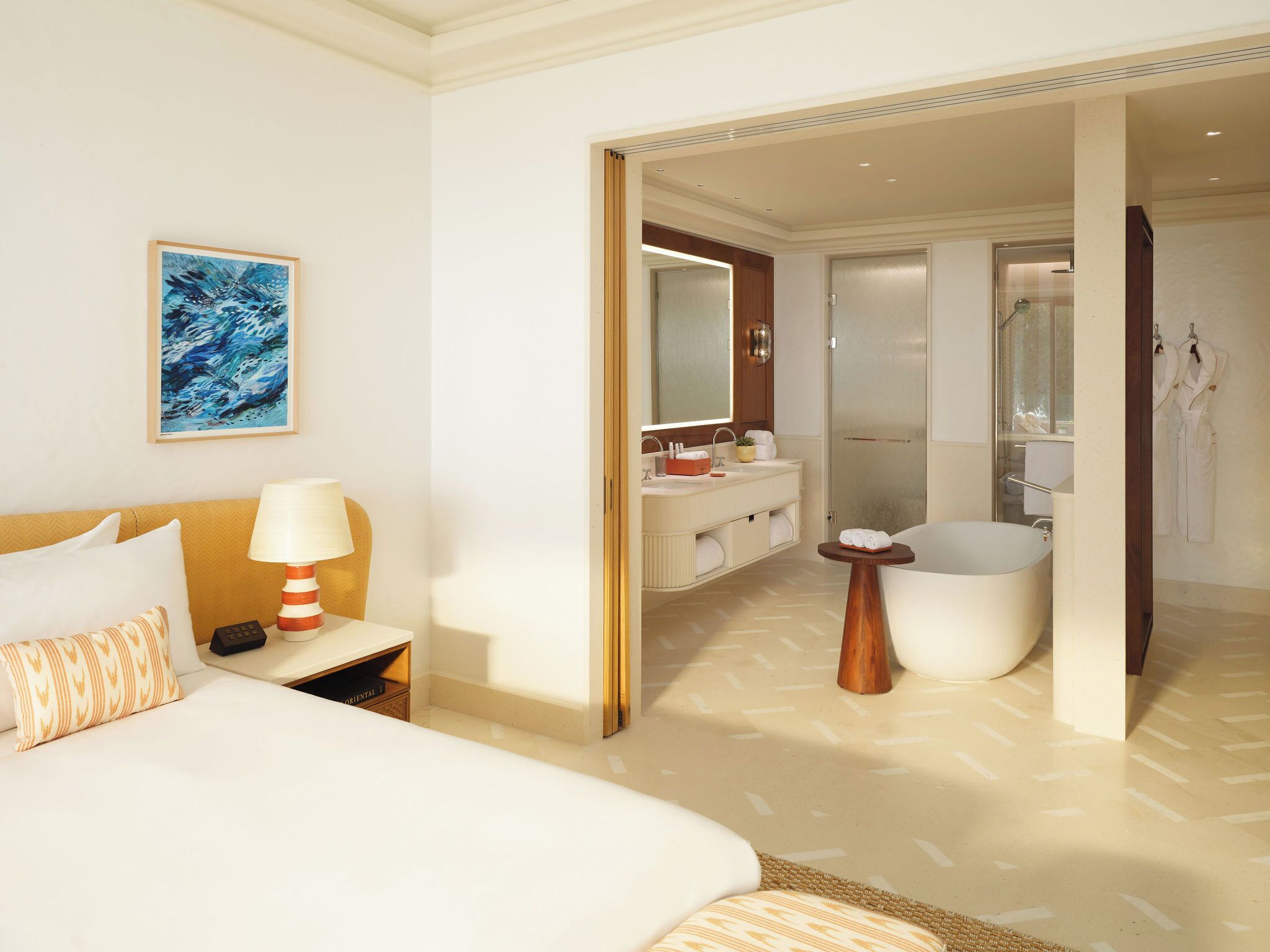 Habitación de hotel con cama, mesita de noche, lámpara, obras de arte, baño con bañera y zona de ducha.