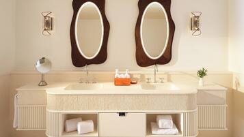 A bathroom with two large mirrors, a sink with two faucets, a small round mirror, and a potted plant.