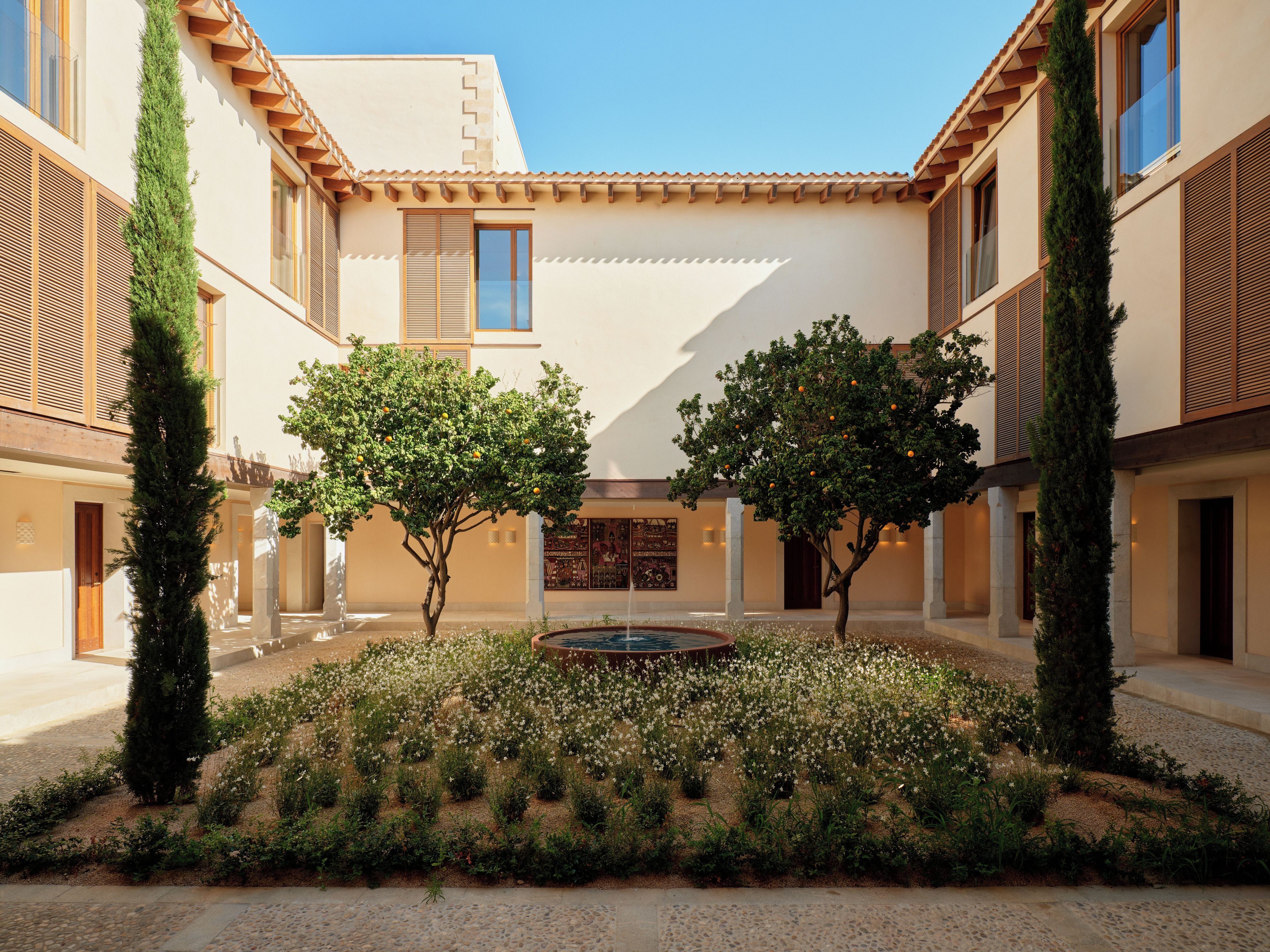 A courtyard with a fountain, surrounded by trees and a building with a tiled roof.