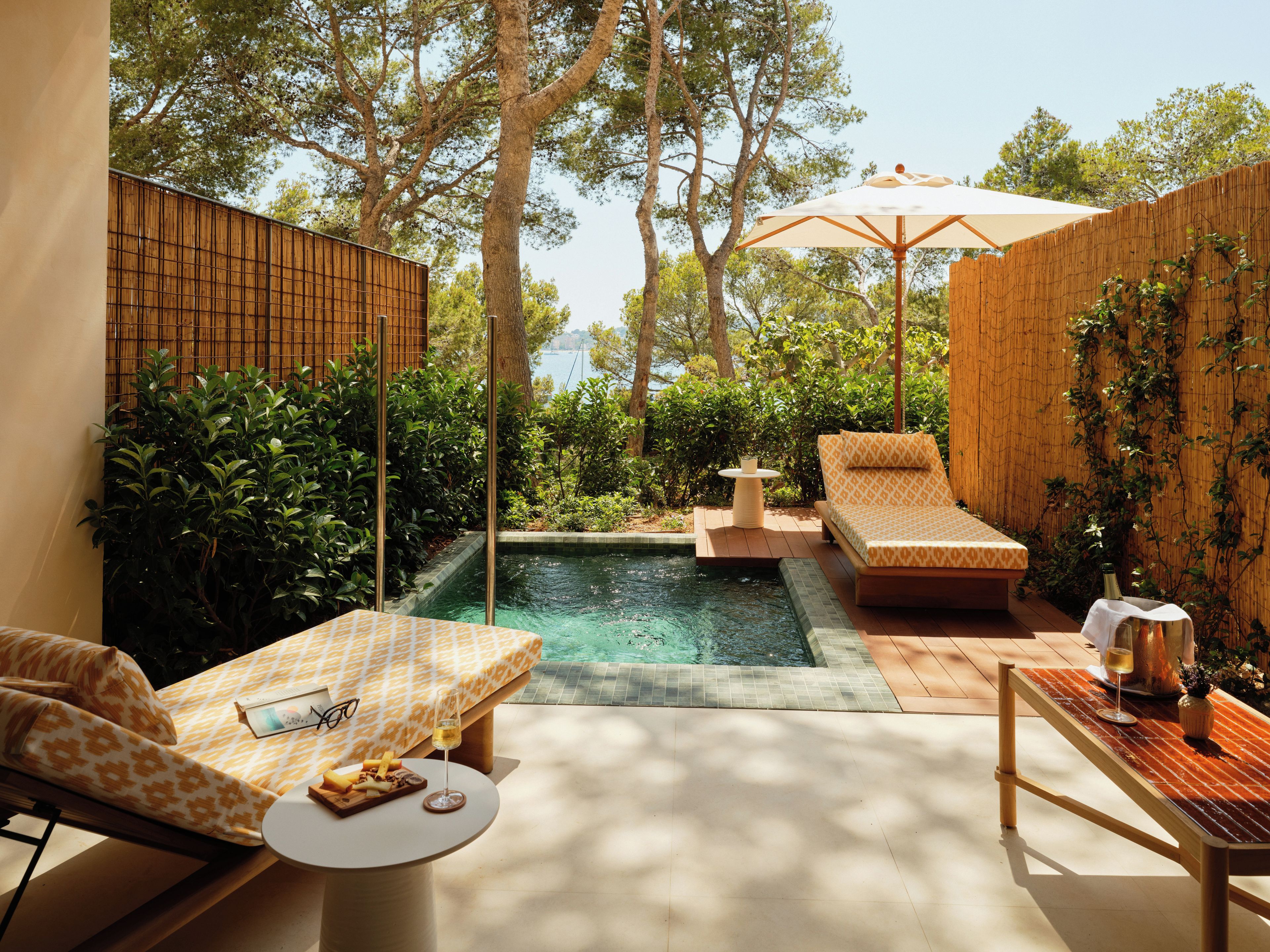 A poolside area with a lounge chair, a small table with a bottle and glass, and a wooden bench.