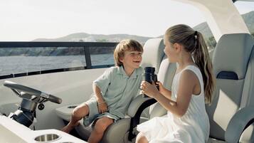 A boat interior with two passengers, a steering wheel, and a view of the water.