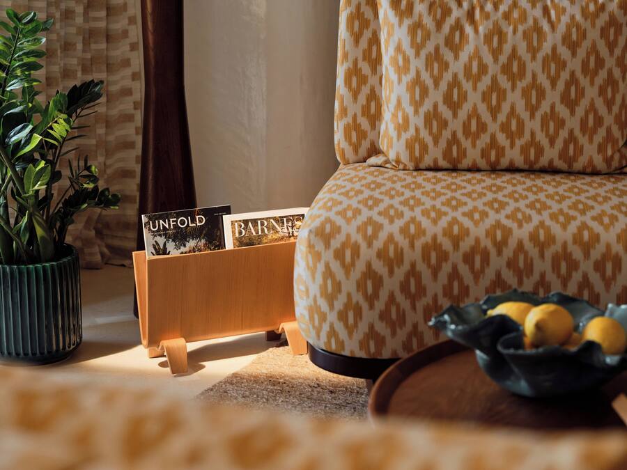 Uma sala de estar aconchegante com um sofá estampado, uma mesa de apoio de madeira com revistas, uma planta em vaso e uma tigela de limões.