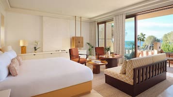 A hotel room with a large bed, a sofa, a chair, a small table, and a view of the sea.