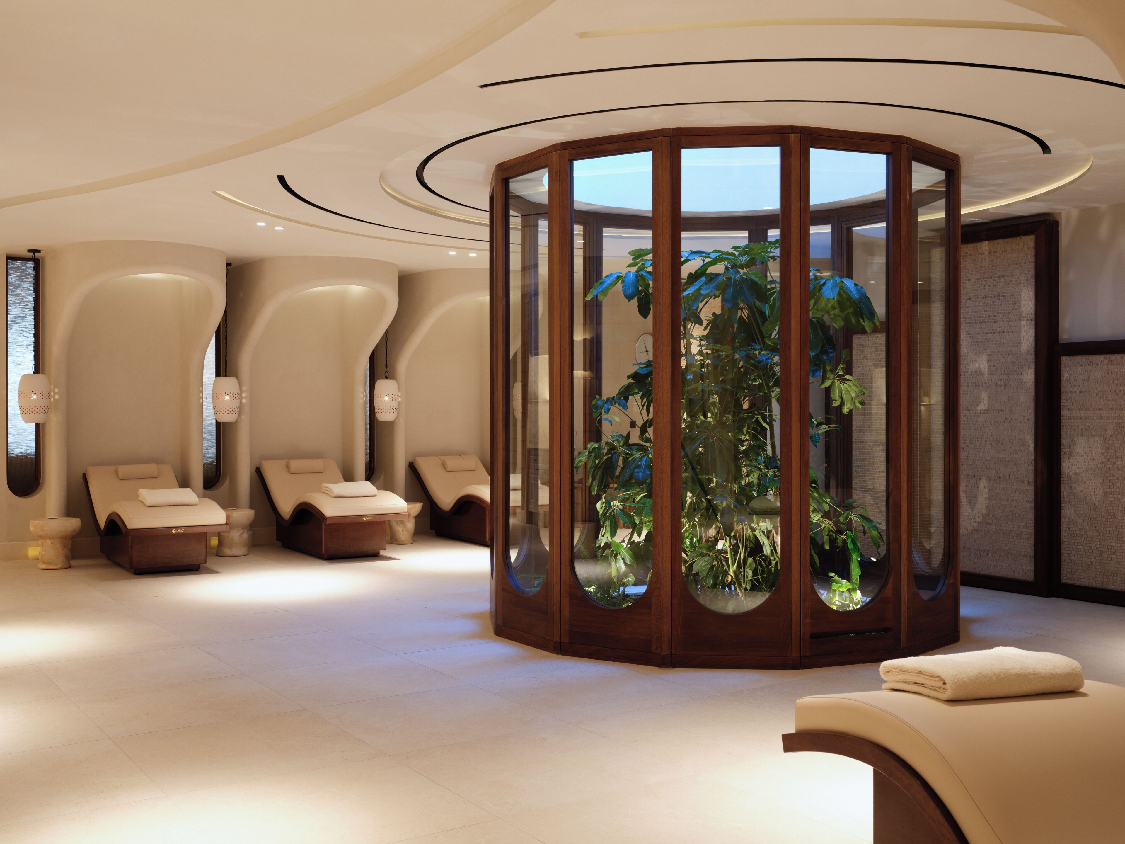 A spa room with a circular wooden structure containing plants, two massage chairs, and a large mirror.